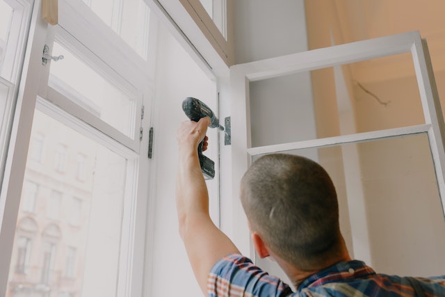 contractor using an electric drill to fix a window hinge